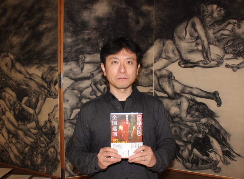 原爆の図第5部「少年少女」の前で、著書を手にする岡村さん=丸木美術館で