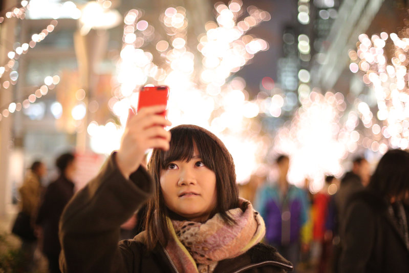 カップルなどでにぎわう中、ソロ活しながらクリスマスイブのイルミネーションを楽しみ、スマートフォンで「自撮り」する朝井麻由美さん(中央)=東京・丸の内で2015年12月24日、後藤由耶撮影