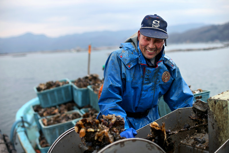 水を浴びながら、長面浦のいかだからカキを引き上げ、船に積み込む西村久治さん=宮城県石巻市で2016年2月20日、森田剛史撮影