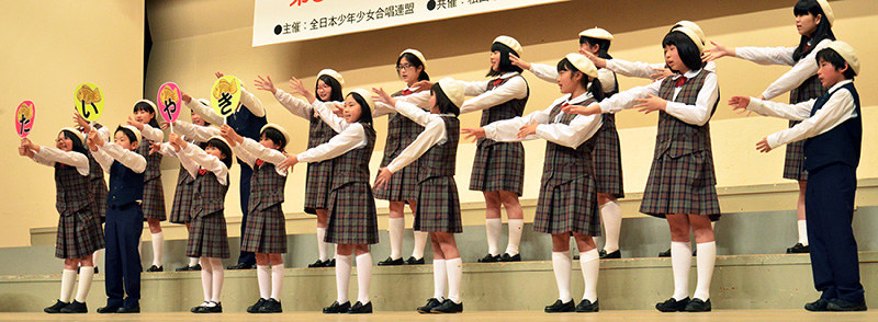 振り付けを交えて元気な声を響かせる子供たち=松山市民会館で