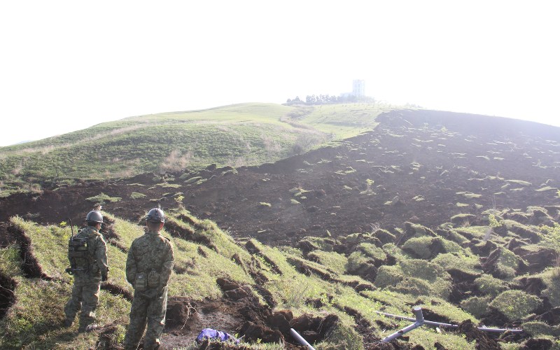 朝日が昇る高野台団地の丘を見上げる自衛官たち。土砂が流れ下った部分(右側)は芝がはげ、土がむき出しだった=熊本県南阿蘇村河陽で2016年4月19日午前7時53分、田畠広景撮影