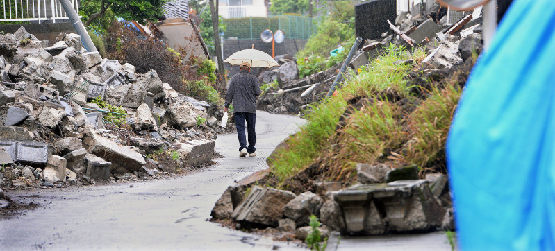 雨の降る中、崩れた住宅地の間を歩く男性=熊本県益城町で2016年5月10日、小関勉撮影