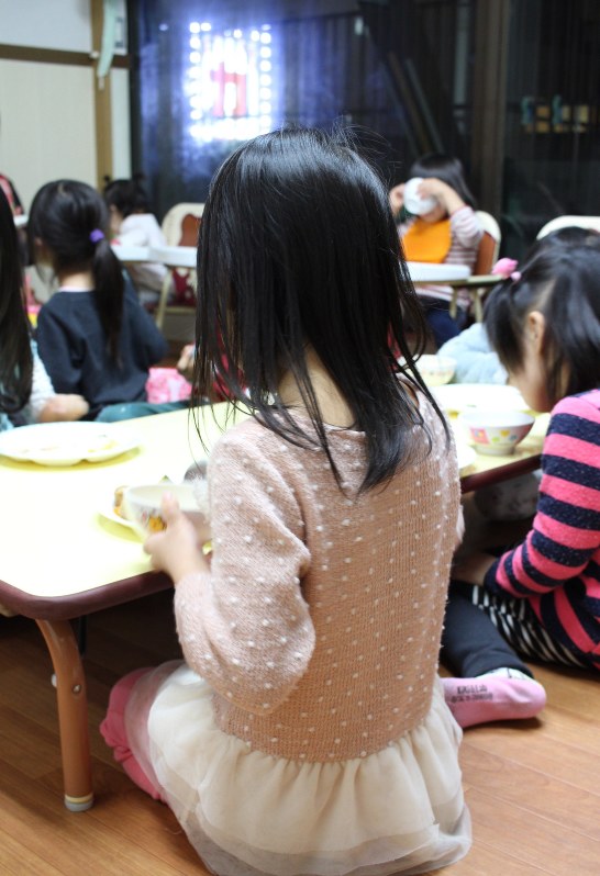 雑居ビル6階にある一室で夕食を取る子どもたち。外にカラオケ店のネオンが光る=千葉県松戸市の「ミルキーホーム松戸園」で、宇多川はるか撮影