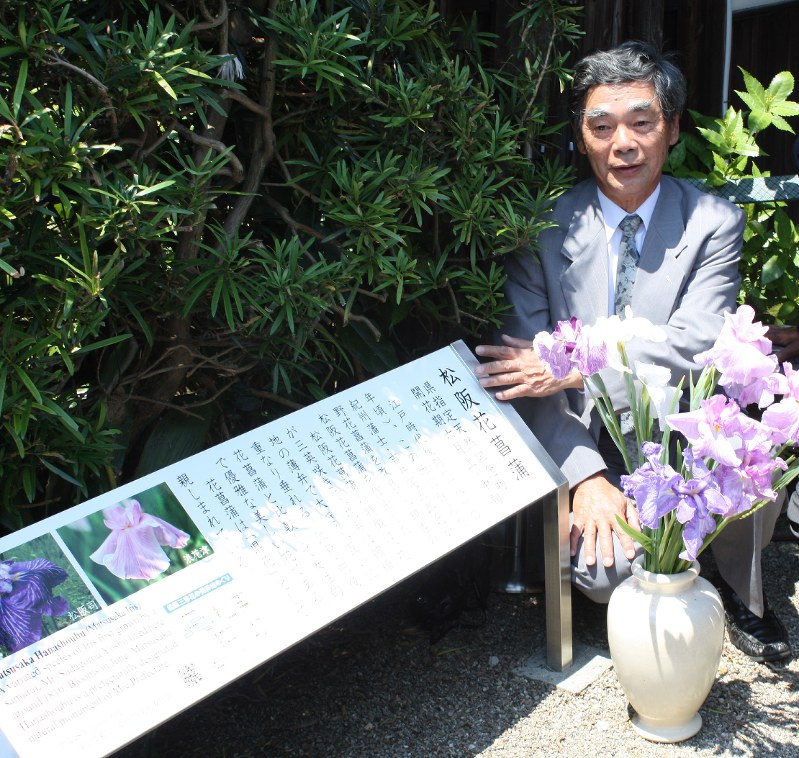 自宅玄関の横に建てられた碑を前に、花の歴史を語る吉井捷雄さん=松阪市殿町で