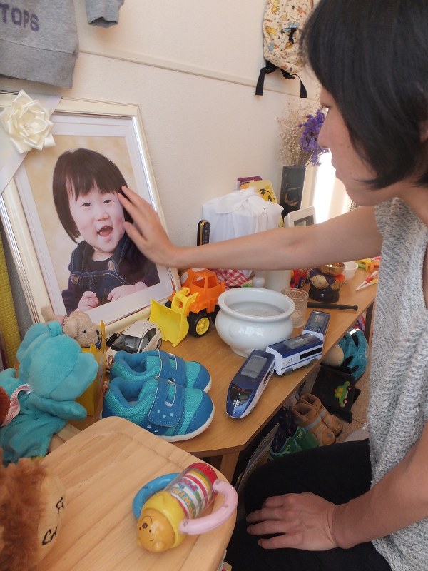 賢人ちゃんの遺影をなでる母親。入所する直前に歩き始めたばかりで、用意していた靴(手前)は一度も履くことができなかった=千葉県内の自宅で2016年6月22日午前4時半、黒田阿紗子撮影