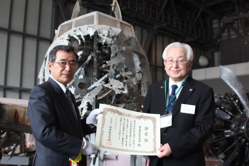 一式双発高等練習機の前で、認定証を受け取った大柳繁造館長(右)と日本航空協会の久保小七郎副会長=三沢市の県立三沢航空科学館で