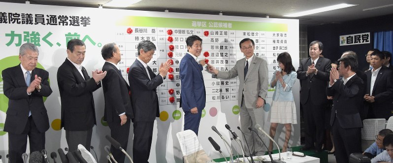 自民党執行部が拍手する中、候補者ボードの当確者名にバラを付ける安倍晋三首相(中央)と谷垣禎一幹事長(同右)=東京都千代田区で2016年7月10日午後9時46分、藤井太郎撮影