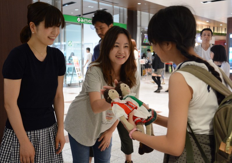 オーストラリアに向かう出発式で児童に人形を手渡す佐藤美香さん(中央)=JR仙台駅で