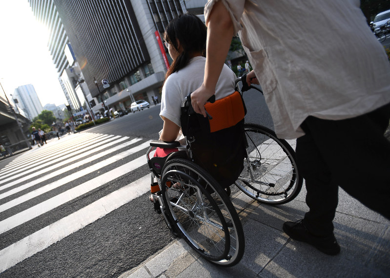 母親に付き添われ車椅子で外出する女子生徒。長時間の外出や体調不良の時は車椅子が欠かせない=大阪市北区で2016年7月21日、久保玲撮影