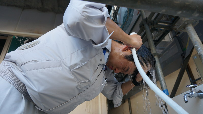 マンション建設現場の一角に据えられたシャワーを使い、水で頭を洗う財津さん。水浴びで体温を下げる効果が期待できる