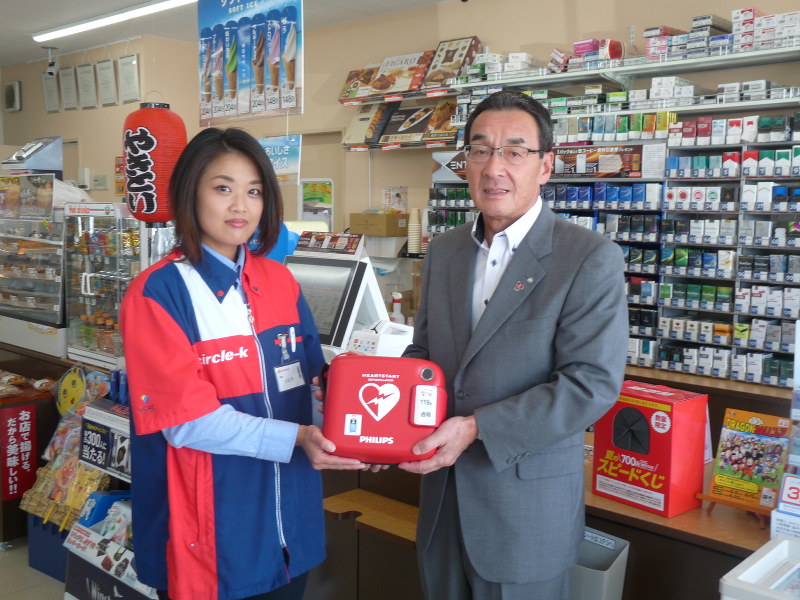 伊藤楓店長(左)にAEDを手渡す谷村町長=神戸町で