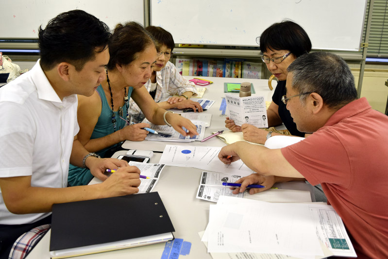 外国人のための4言語によるお薬手帳の試作品を見ながら話し合う大川印刷と共生のまちづくりネットワークよこはまの関係者ら=横浜市神奈川区で、石塚淳子撮影