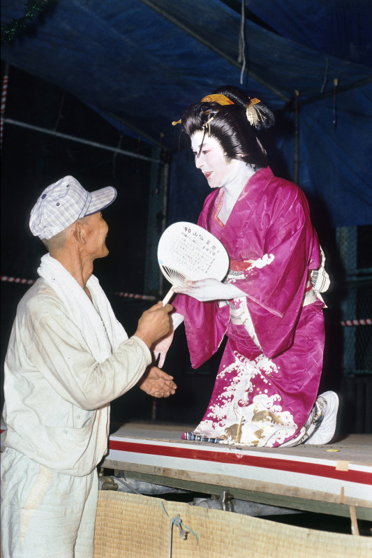 1990年の山谷の夏祭りで舞踊ショーを終え、駆け寄ってきた労働者と握手をする玉ちゃん=フォトジャーナリストの大島俊一さん撮影