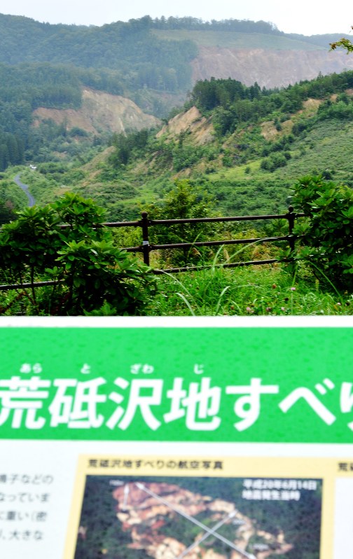大規模な崖崩れ跡(右奥)が残る「荒砥沢」のジオサイト。掲示板(手前)は設置されたが、住民からは「間に山もあり、ここからでは全体像が伝わらない」との指摘も=栗原市の藍染湖公園で