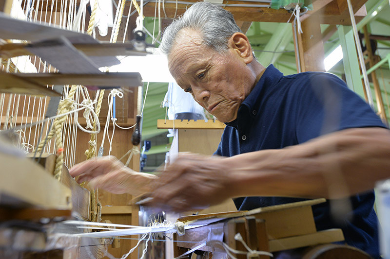両手を素早く動かして帯を織る岩間利夫さん=京都市上京区の龍村美術織物烏丸工場で、小松雄介撮影