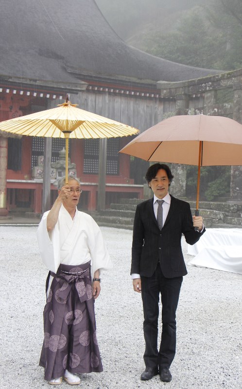 奉幣殿をバックに高千穂宮司(左)と記念撮影に応じる東儀さん