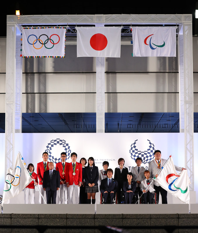 東京都庁前に掲揚された五輪旗(左上)とパラリンピック旗(右上)の前に整列したオリンピアンとパラリンピアン=東京都新宿区で2016年9月21日午後7時42分、小川昌宏撮影