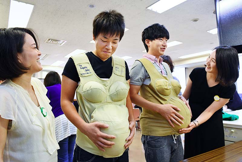 これから親になる人を対象に大阪府高槻市が毎月開いている「ママパパ教室」で、妻が見守る中、妊婦体験ジャケットを着用する夫たち=2016年9月16日、大西岳彦撮影