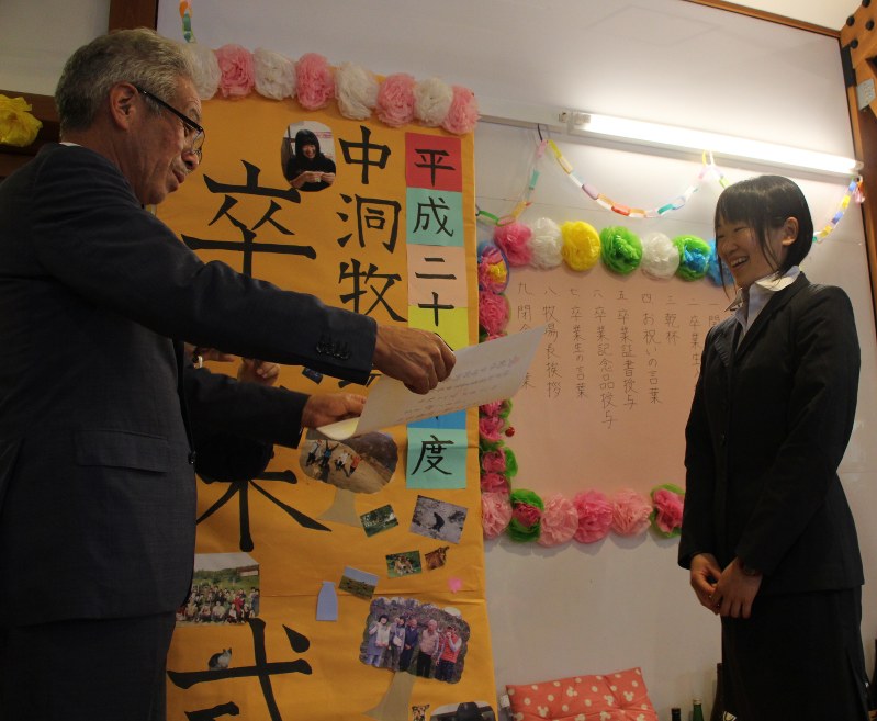 牧場長の中洞正さん(左)から卒業証書を渡される島崎薫さん=岩泉町上有芸の中洞牧場で