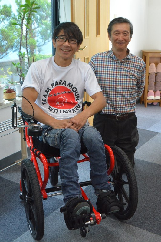 レースに使うものと同型の車椅子に乗る猪飼嘉司さん(左)と西田実喜さん。レースでは猪飼さんが電極を脚に取り付ける=札幌市で
