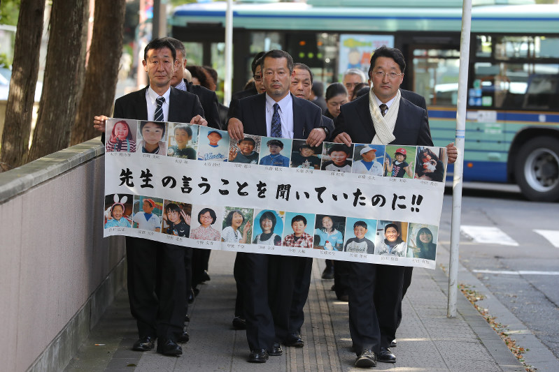 亡くなった大川小の児童たちの顔写真を並べた横断幕を掲げ、仙台地裁に入る遺族ら=仙台市青葉区で2016年10月26日午後1時半、喜屋武真之介撮影