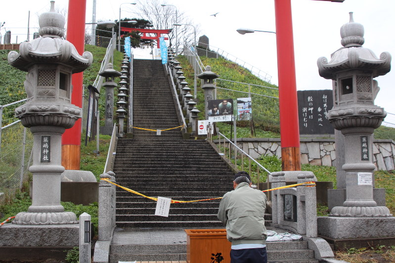 全焼した蕪嶋神社につながる階段の前で手を合わせる参拝客=八戸市鮫町の蕪嶋神社で