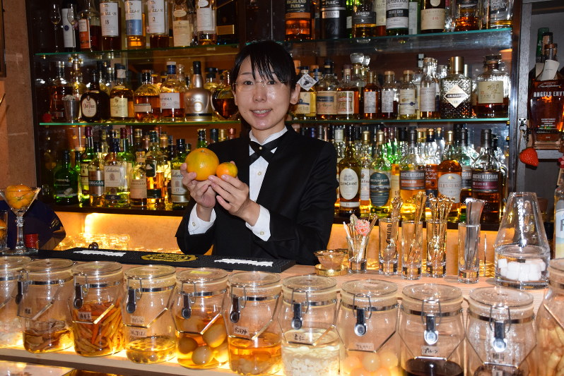 国見みかんを手に県産にこだわったリキュールの開発に意欲を示す原百合子さん=宇都宮市本町の「BAR フルールドゥリス」で
