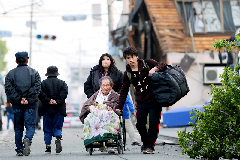 災害時には迅速な情報発信が不可欠だ。熊本地震でがれきが散乱する中、車椅子を押しながら避難する人たち=熊本県益城町で2016年4月16日