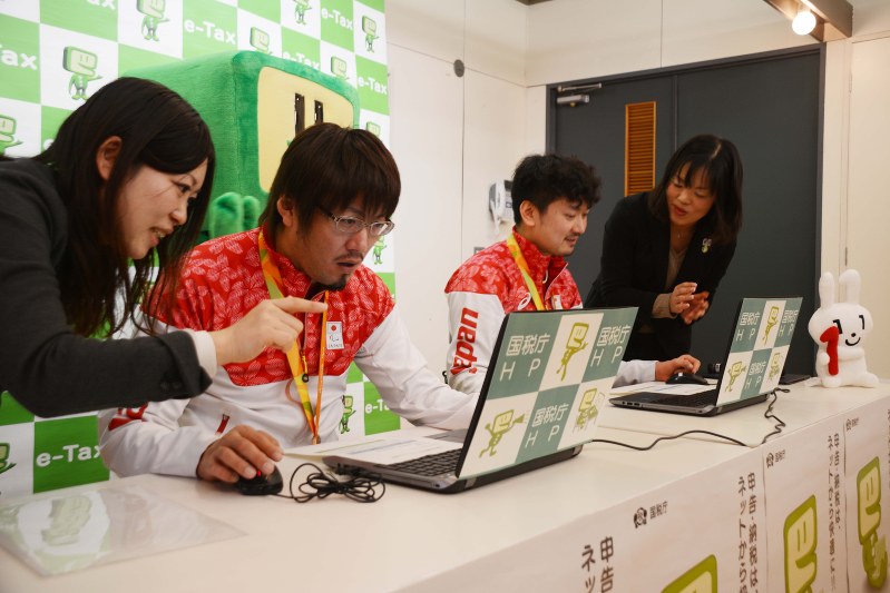 電子申告を模擬体験する池崎選手(左から2人目)と今井選手(同3人目)=渋谷区内で