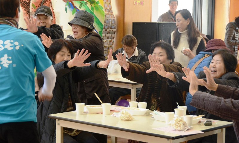 交流会の「笑いヨガ」コーナーで、両腕を前に出して大声で笑う参加者たち