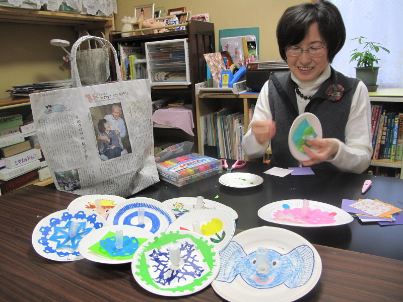 市販の弁当についているしょうゆ入れと紙皿でコマを作る田中さん。紙皿の中心に穴を開け、しょうゆ入れを刺し、裏側からふたを留めただけ。皿に絵を描いたり切り絵を張ったりして、くるくる回して遊ぶ