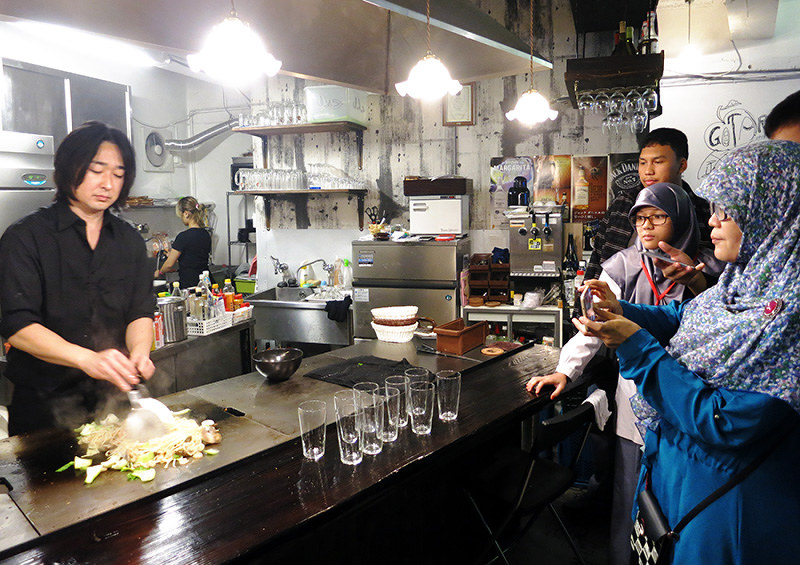 ハラールのメニューがある鉄板焼き店で、焼きそばを作る様子を興味津々で見つめる一行=東京都台東区で、中本泰代撮影