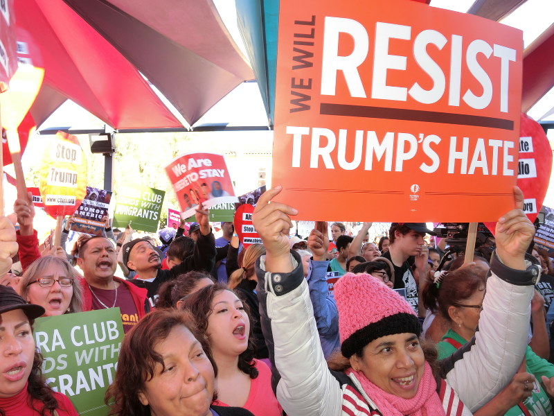 「私たちはトランプ氏の憎しみに抵抗する」「私たちはここにいて、ここにとどまる」などと書かれたプラカードを掲げて移民を守る集会に参加した人々=米ロサンゼルスで14日、長野宏美撮影