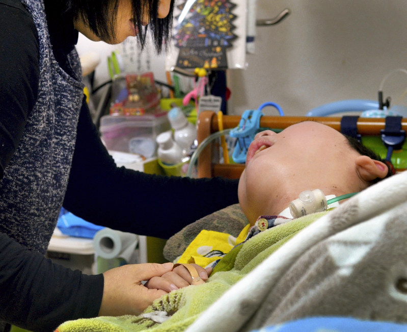 事故で寝たきりとなった少年に語りかける母親。少年は事故でコミュニケーション能力を失い、呼びかけに答えることもできなくなった=福岡県で