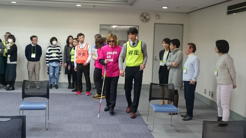 白杖を手に誘導の見本を見せる高橋勇市さん=千代田区で