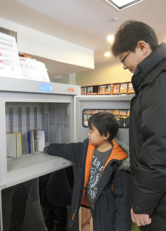 書籍消毒機を使う親子=東京都新宿区戸山図書館で、池乗有衣撮影