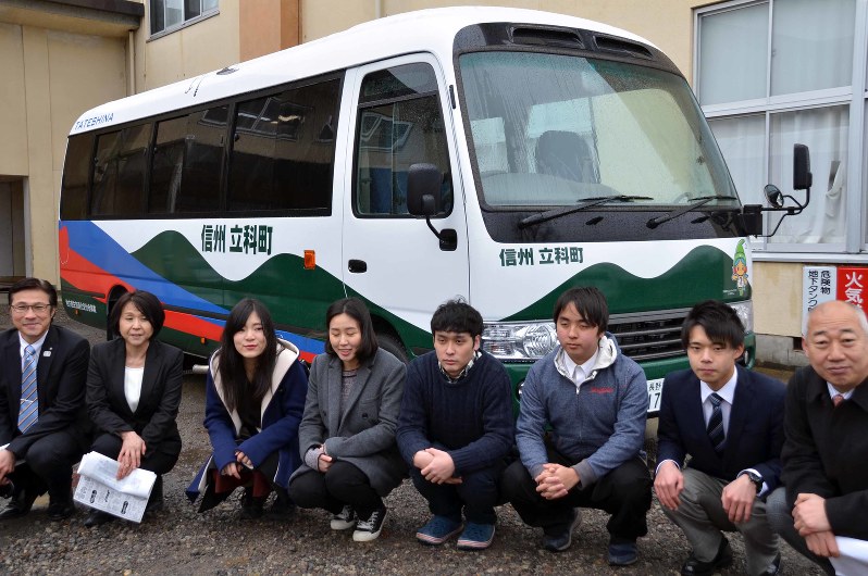 お披露目されたバス(後方)をデザインした蓼科高校生徒と長野大学学生ら=立科町の蓼科高校で