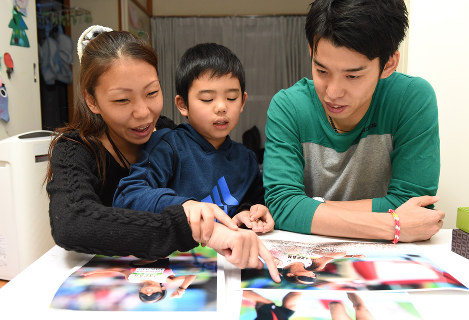 千明（左）が出場したリオデジャネイロ・パラリンピックの写真を眺める裕士（右）と諭樹さん。諭樹さんが千明の手を取り「これはママが踏み切る写真」「こっちは着地したところ。砂がバッと上がってるよ」と説明した＝徳野仁子撮影