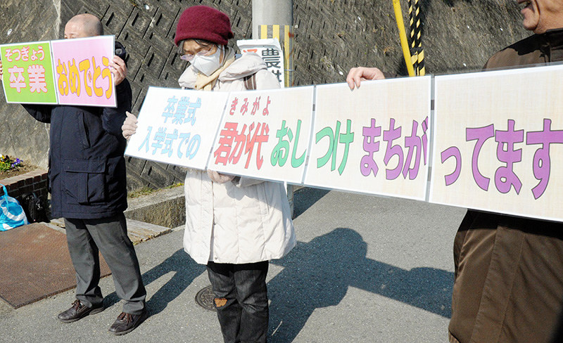 君が代起立斉唱の強制はおかしいとカードを掲げて意思表示する、処分された教員の支援者ら=大阪府茨木市で2017年3月、湯谷茂樹撮影