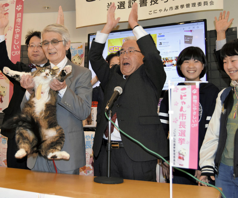 こにゃん市史上初の再選を果たし、飼い主の豊永さんに抱きかかえられてバンザイするジュリアーノ(左)=滋賀県湖南市岩根の十二坊温泉ゆららで2017年4月23日、衛藤達生撮影