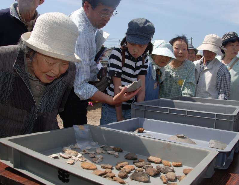 災害公営住宅の建設用地から見つかった土器に見入る地元の地元のお年寄りや家族連れ=2013年5月、中尾卓英撮影