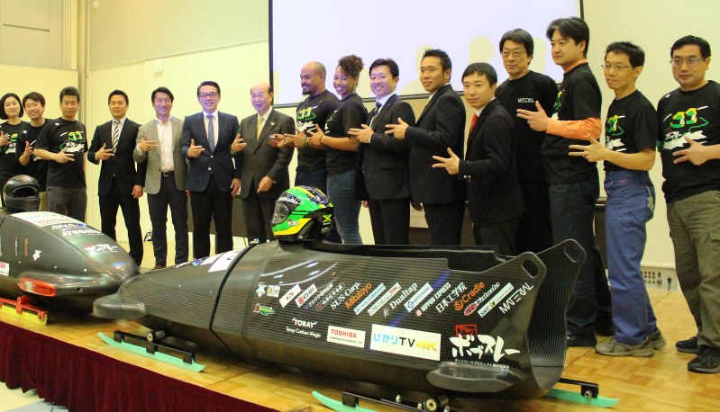 下町ボブスレーの最新型(右)と1号機を前に笑顔を見せるジャズミン・フェンレイタービクトリアン選手(中央)とプロジェクトのメンバーら=大田区南蒲田1の大田区産業プラザで