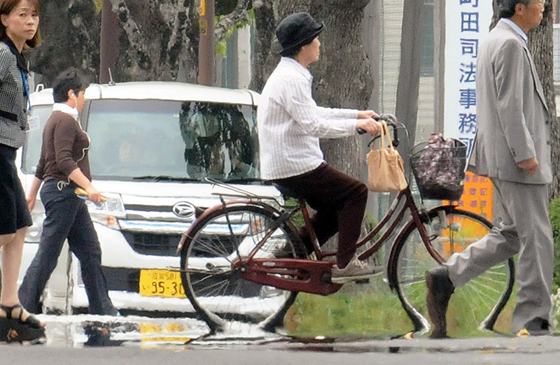「逃げ水」現象で、道路面に溶け込むように見える自転車のタイヤや人の足=滋賀県東近江市八日市緑町で、金子裕次郎撮影
