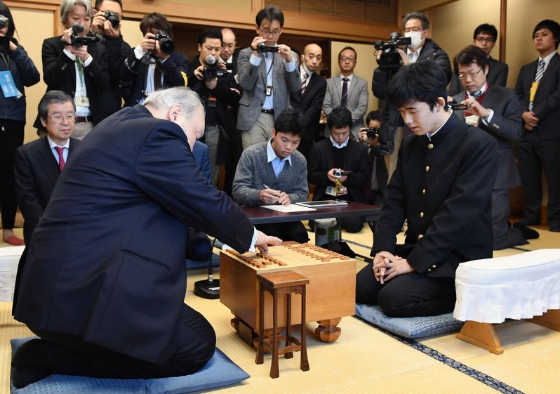 初手を指す加藤一二三九段（左）。右は藤井聡太四段＝東京都渋谷区の将棋会館で２０１６年１２月２４日午前１０時、猪飼健史撮影