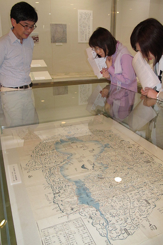 滋賀大経済学部付属史料館の青柳館長(左)から江戸時代の滋賀県観光案内絵図の説明を受ける見学者ら=滋賀県彦根市馬場1の同大で、西村浩一撮影