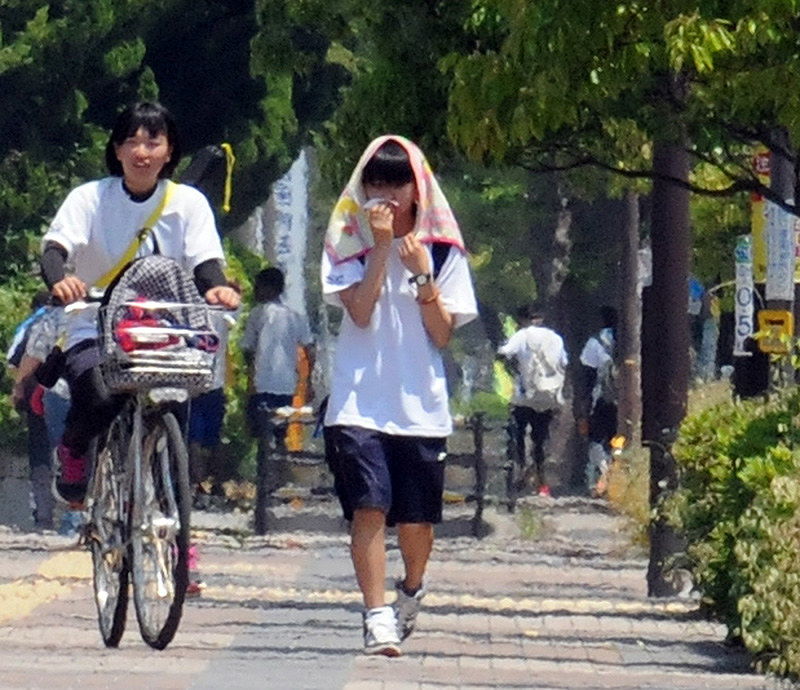 暑さで空気が揺らめく中、タオルで日差しをよけながら帰宅する高校生=滋賀県東近江市八日市東浜町で、金子裕次郎撮影