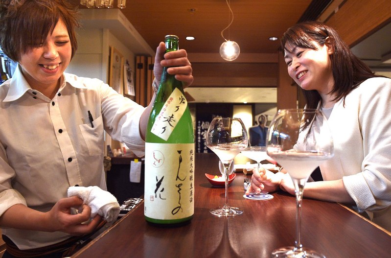 店員の西山佳那さん(左)に薦められた秋田県産の日本酒を楽しむ倉嶋紀和子さん=東京・丸の内で2017年5月22日、丸山博撮影