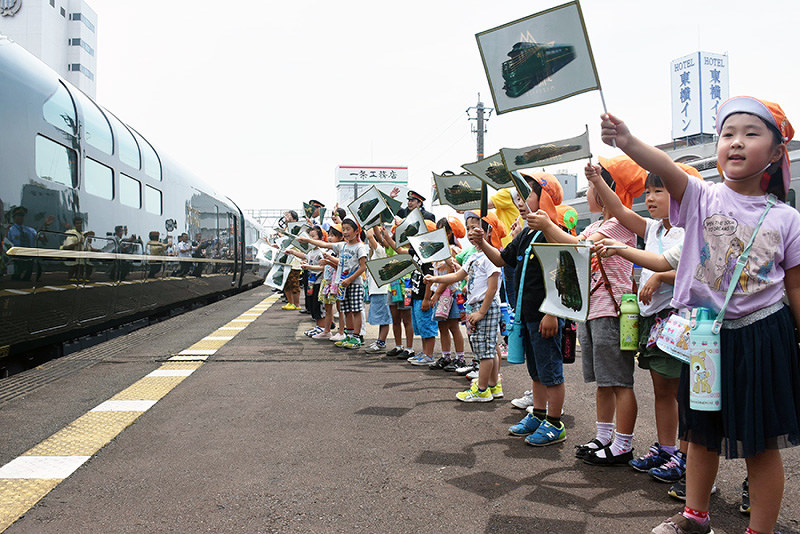 瑞風の乗客に向かって旗を振る子供たち=鳥取市のJR鳥取駅で、園部仁史撮影