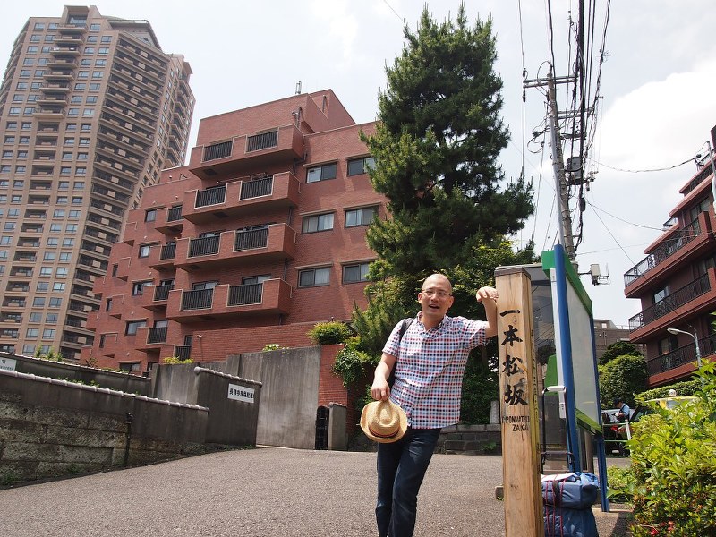 一本松で一息入れる一之輔さん。左手には現代のランドマーク、元麻布ヒルズフォレストタワーがそびえる=東京都港区元麻布で
