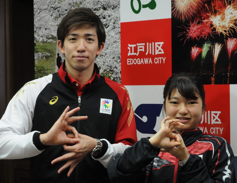 デフリンピックのロゴマークを手で表す茨選手(左)と高岡選手=江戸川区役所で
